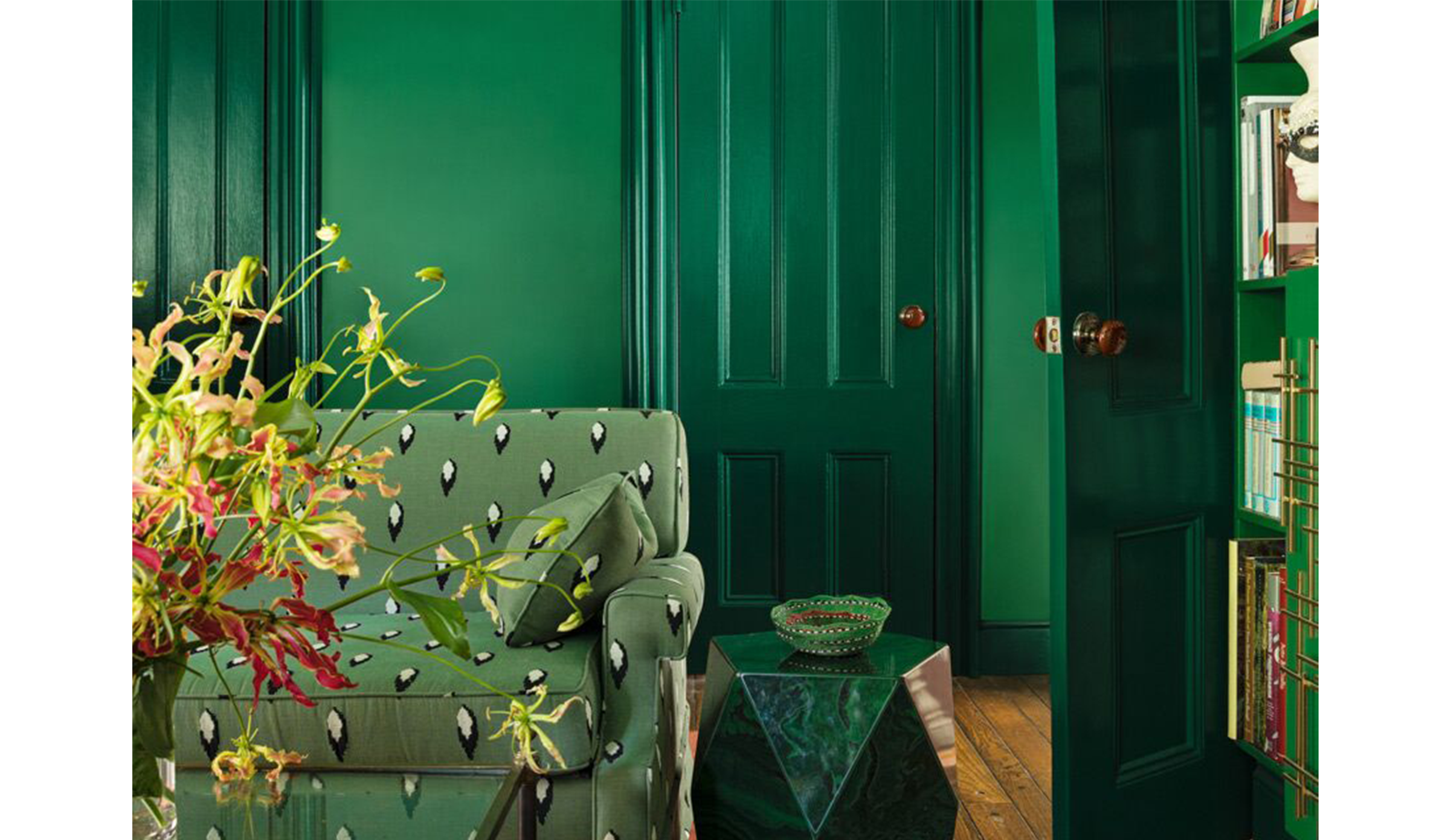 Sala verde con sofá estampado, mesa auxiliar de piedra, mesa de café de cristal y estanterías a jueg