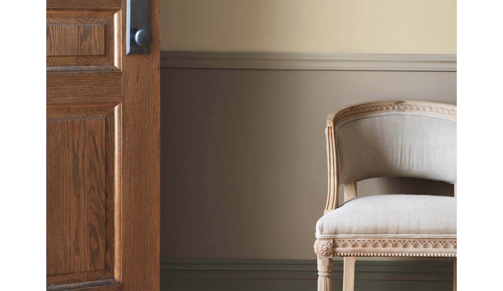 Vestíbulo color taupe con puerta de madera, lambriz beige y silla.