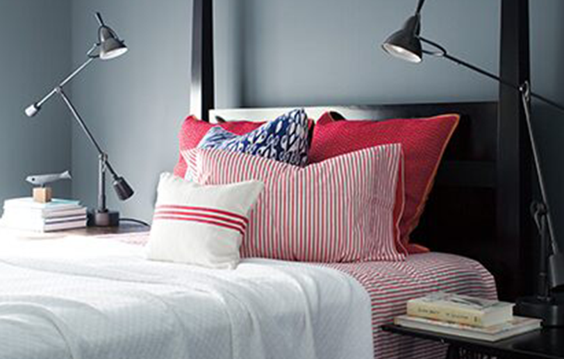 Dormitorio gris lobo elegante c/ cama negra, ropa de cama roja y blanca, 2 lámparas de pared.