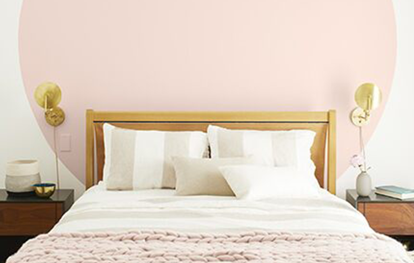 Dormitorio claro con paredes blancas, círculo rosa detrás de la cama blanca con manta rosa y lámpara