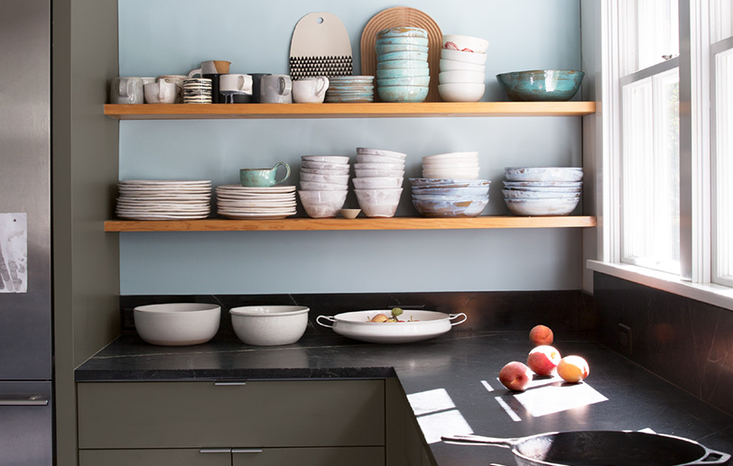 Cocina con 2 estantes de madera que exhiben tazones y platos en una pared de color azul claro.