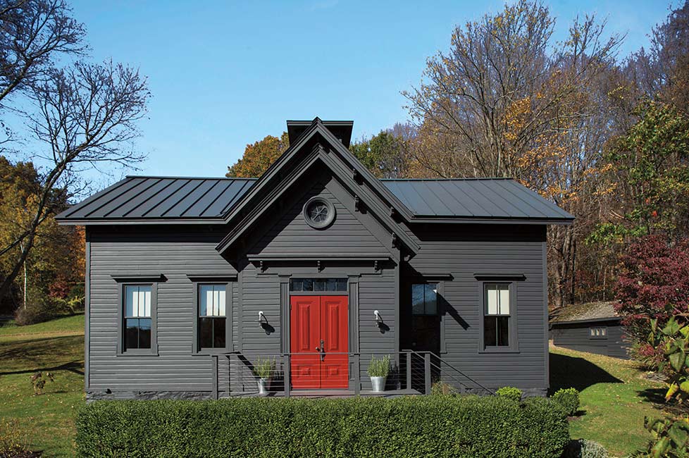 Una casa pintada de gris oscuro con una brillante puerta delantera roja, un seto frontal