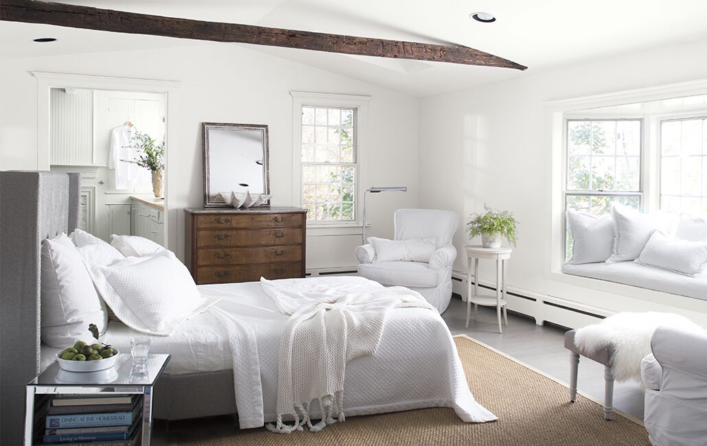 Acogedora habitación blanca con ropa de cama, sillas, ventana de bahía, cómoda antigua, techo