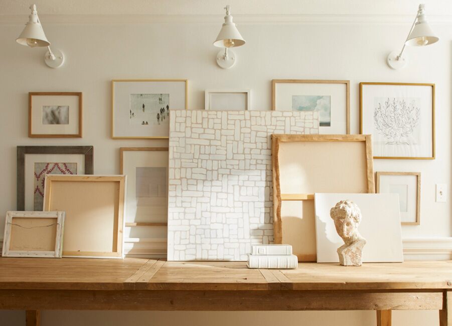 Pared galería blanca con matiz rosado, mesa de consola madera, marcos arte y apliques blanco crema.