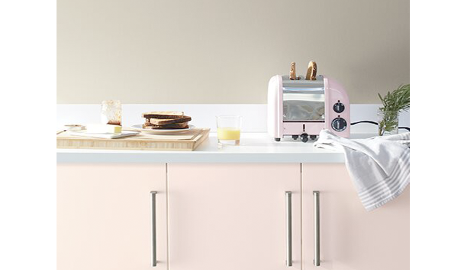 Paredes de color greige con gabinetes de color rosa claro y encimeras blancas en la cocina.