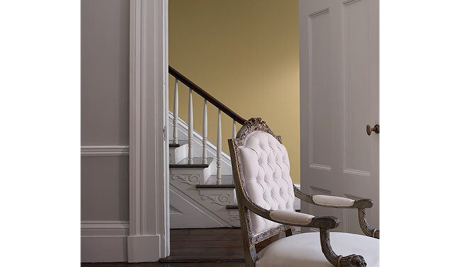 Una sala de estar en gris claro cuenta con una puerta que se abre a un vestíbulo pintado de amarillo