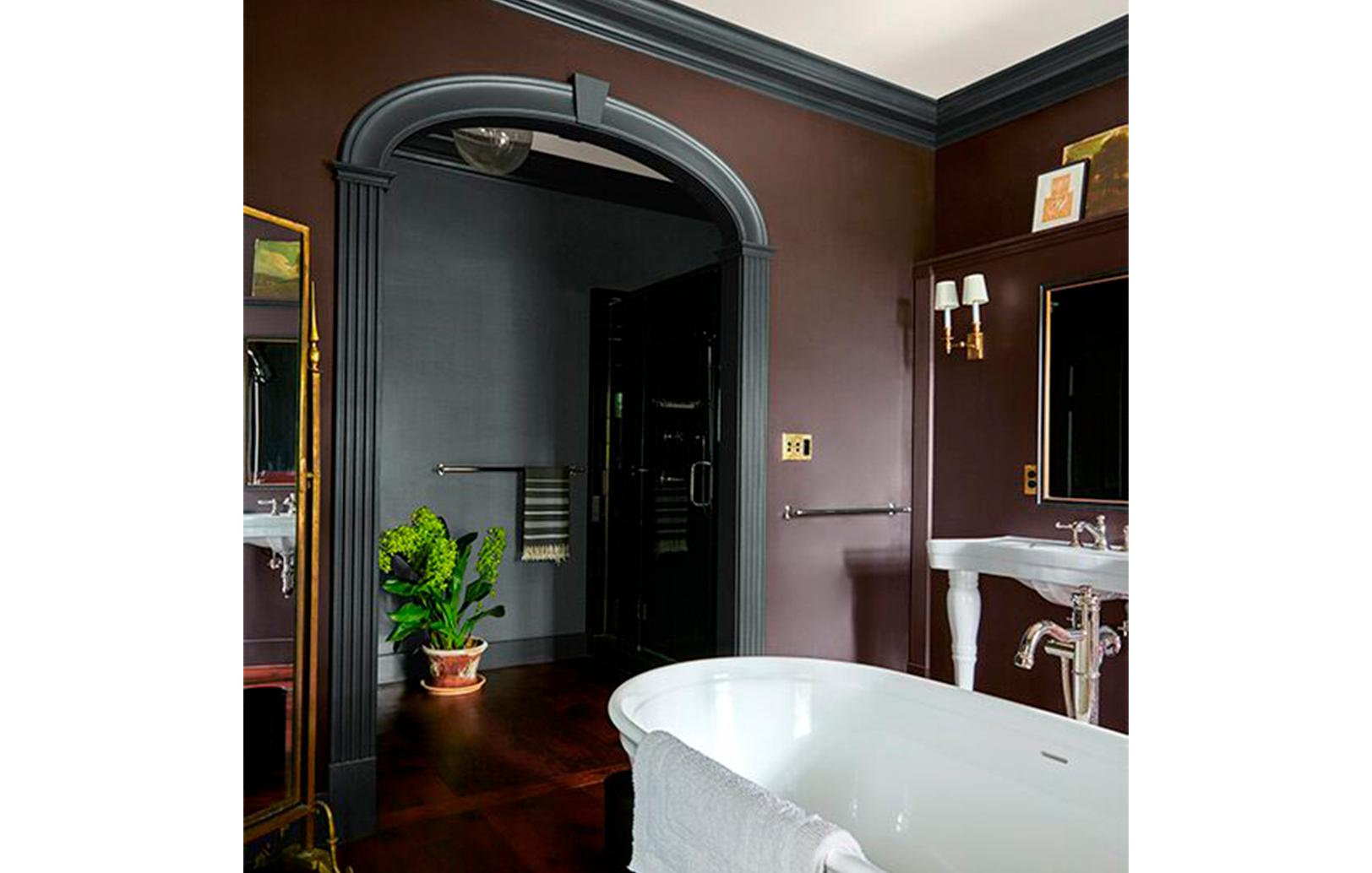 Un gran baño con paredes de color marrón oscuro y molduras negras, bañera profunda y detalles dorado
