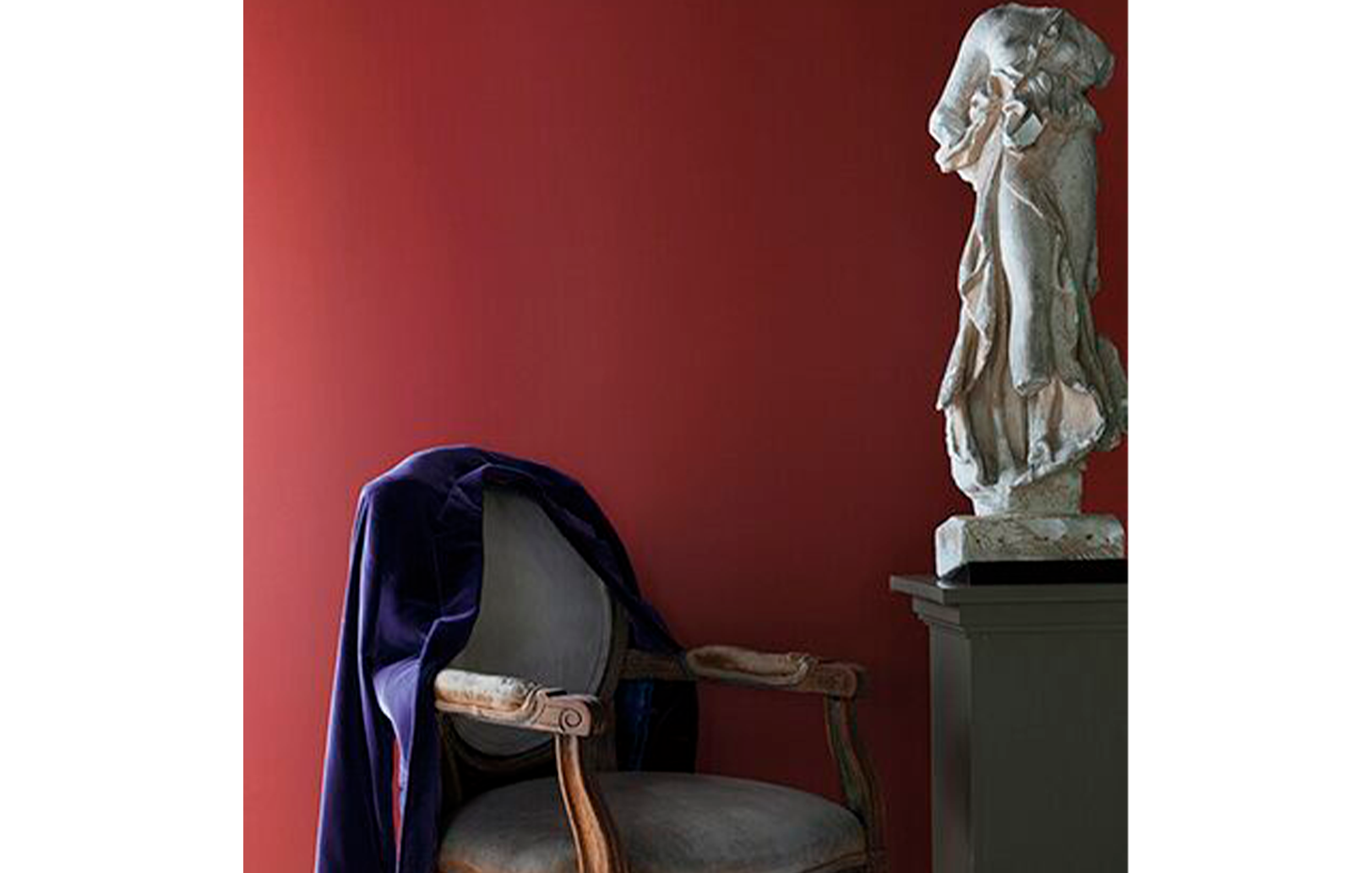Pared pintada de rojo detrás de una estatua blanca sobre un pedestal y una silla tradicional