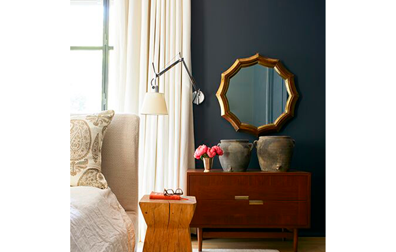 Un dormitorio pintado de negro con cama crema, mesas decorativas de madera con macetas y flores