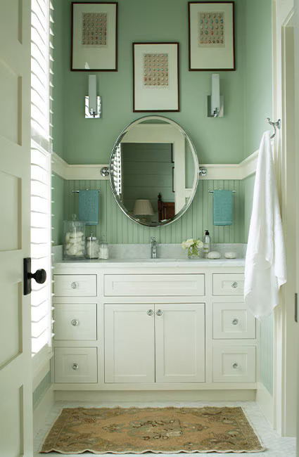 Seafoam green bathroom with circular mirror and three picture frames hanging above a white vanity.